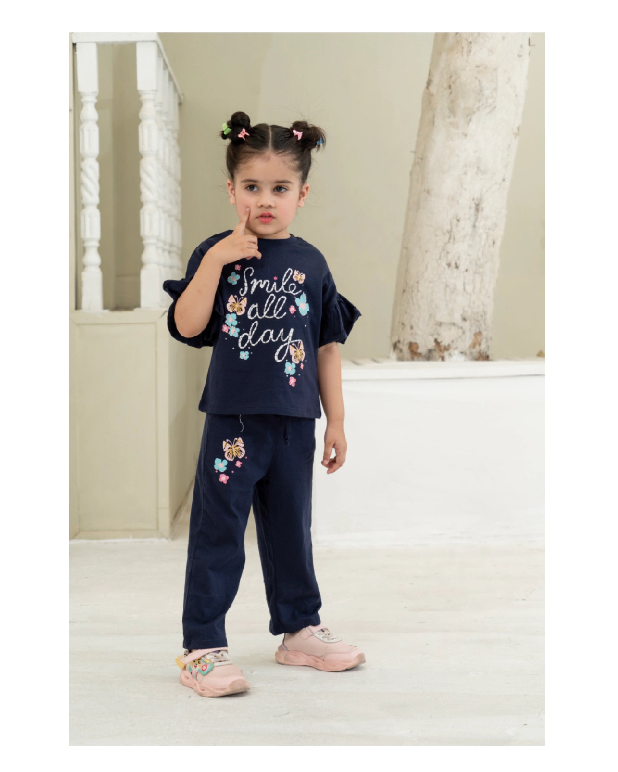 Young girl in navy outfit with floral design and text, standing indoors.